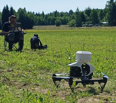 A drone on the ground in a Finnish field with an operator running the flight from a folding chair behind it.